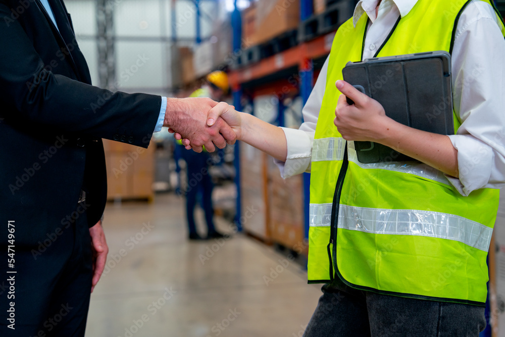 Close up business man and warehouse factory worker shake hands together look like they success about their deal of the project. Close up business man and warehouse factory worker shake hands together look like they success about their deal of the project.