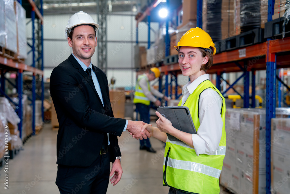Business manager man shake hands to warehouse worker woman with her team work in the background and they also look at camera with smiling. Business manager man shake hands to warehouse worker woman with her team work in the background and they also look at camera with smiling.