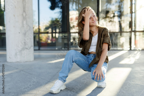 Portrait of teenage girl sitting on floor, urban street, sunlight