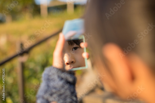 秋の公園で遊んでいる子供が手鏡を見ている様子