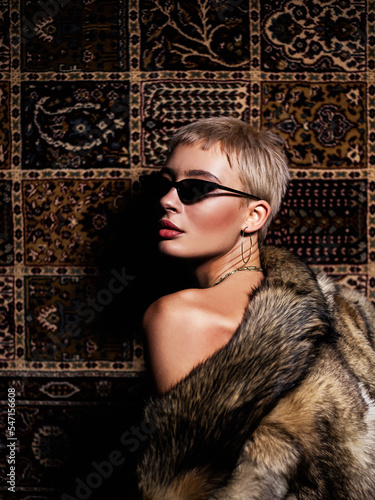 Portrait of a naked woman in sunglasses in a fur coat on the background of a carpet