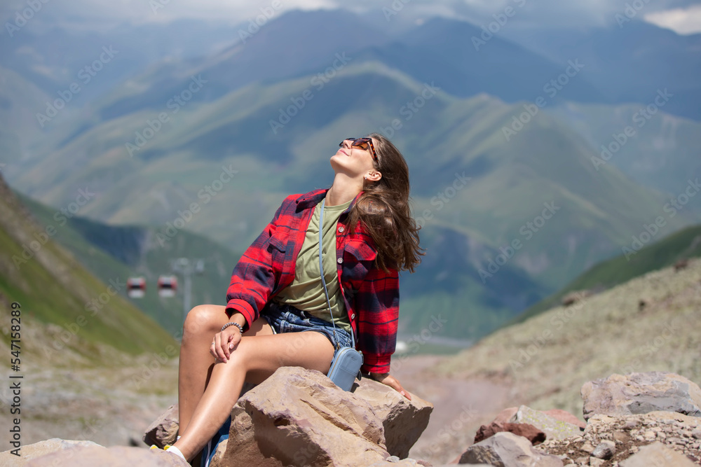 Happy female hiker on the top of the mountain enjoys the beautiful view of the mountains.