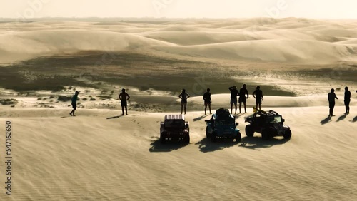 People in silhouette on high sand dune, windy conditions on buggy tour; aerial photo
