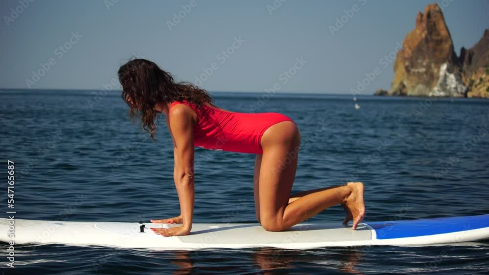 Young woman in red swimsuite doing yoga or pilates on sup board with paddle. Balanced pose - concept of harmony with the nature, free and healthy living. Young woman in red swimsuite doing yoga or pilates on sup board with paddle. Balanced pose - concept of harmony with the nature, free and healthy living.