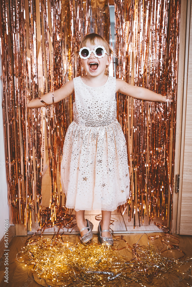 Happy little stylish girl in shiny dress having fun. Festive background  with foil curtain decorations for kids birthday or fancy dress party, disco  music or New Year. Stock-foto | Adobe Stock
