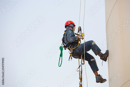 Male worker rope access industrial working at height tank oil wearing harness, helmet safety equipment rope access inspection of thickness tank