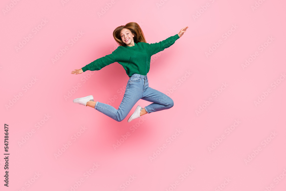 Full length photo of sweet adorable young lady wear green sweater jumping high arms sides isolated pink color background Full length photo of sweet adorable young lady wear green sweater jumping high arms sides isolated pink color background