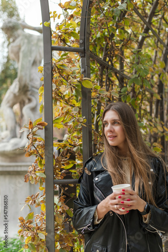 A beautiful woman is drinking hot tea and relaxing in a beautiful autumn park somewhere in Europe.