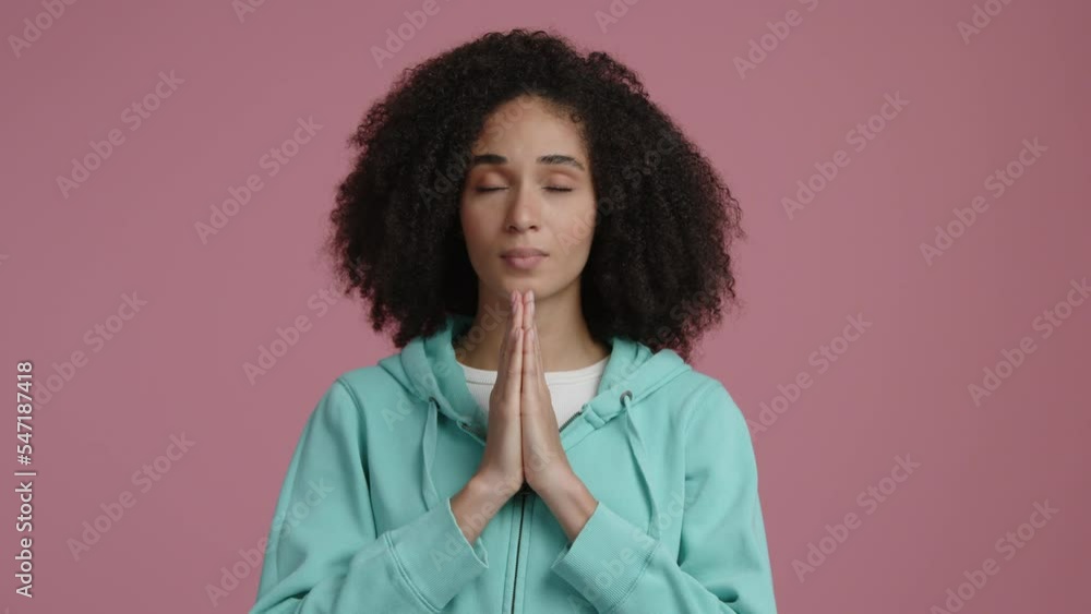 Young lady looking focused while praying. Close-up view of meditating mixed-race woman in casual clothes. High quality 4k footage