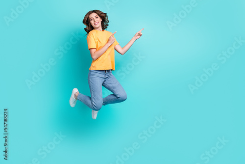 Full length photo of pretty shiny lady wear yellow t-shirt jumping high pointing empty space isolated turquoise color background