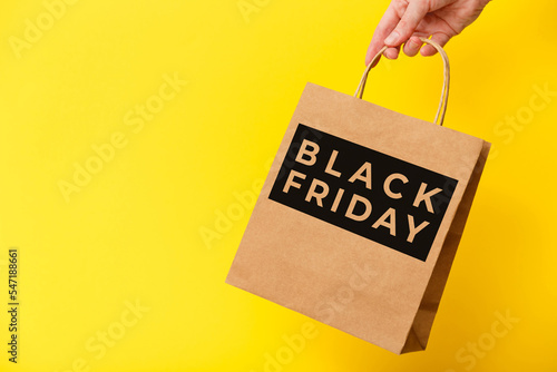 Black Friday, female hand holding brown craft shopping bag on yellow background. Black friday sale, discount, recycling, shopping and ecology concept.