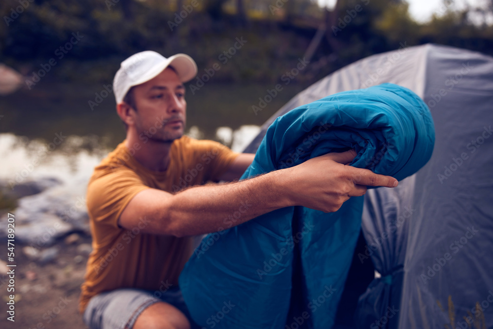 Man camping in nature, setting up the tent for overnight staying near forest river. Man camping in nature, setting up the tent for overnight staying near forest river.