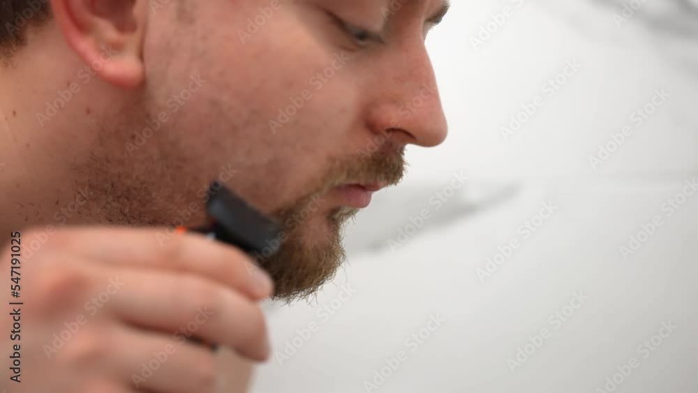 Man with electric trimmer in hands in the bathroom, person shaving beard with electric shaver, skin care routine and grooming concept Man with electric trimmer in hands in the bathroom, person shaving beard with electric shaver, skin care routine and grooming concept
