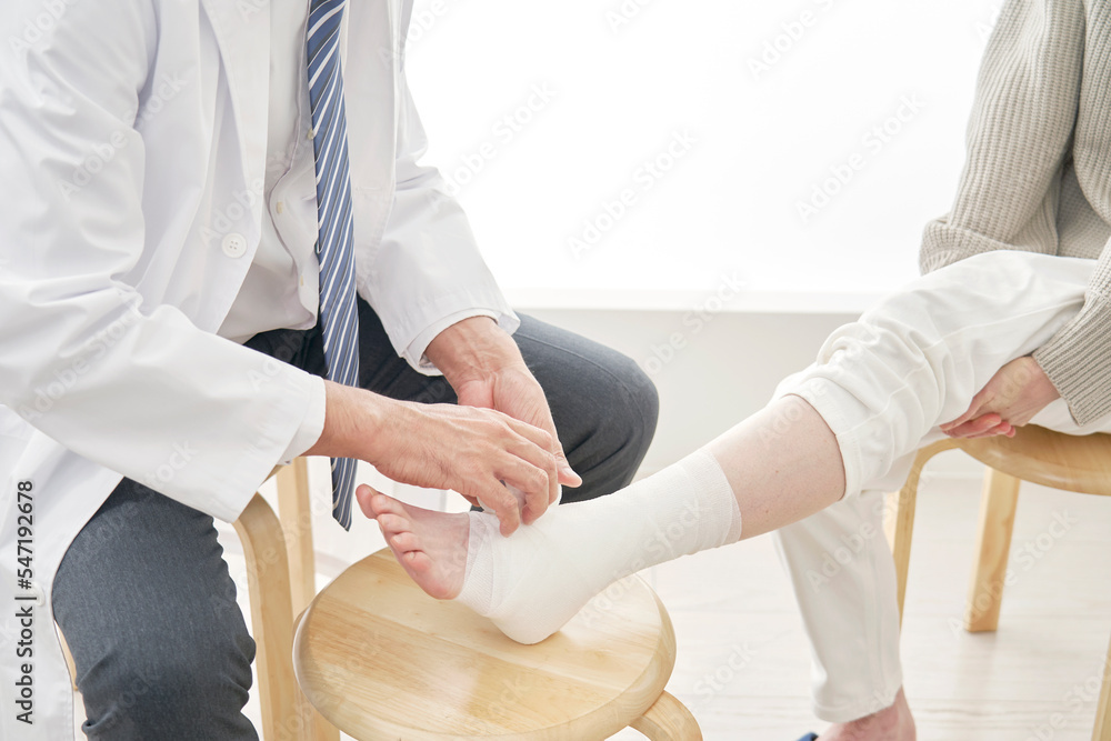 Obraz premium 患者の足首に包帯を巻く医師 顔無し