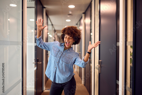 Happy Young Businesswoman Celebrating Dancing Along Corridor In Modern Office
