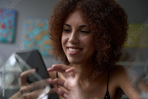 Joyous young lady smiling while looking at screen of smartphone