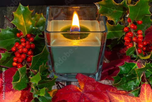 Wallpaper Mural Lit candle in glass vase with holly branches. Christmas decoration. Christmas plants. Green holly leaves and red berries. Red maple leaves. Autumn colors. Torontodigital.ca