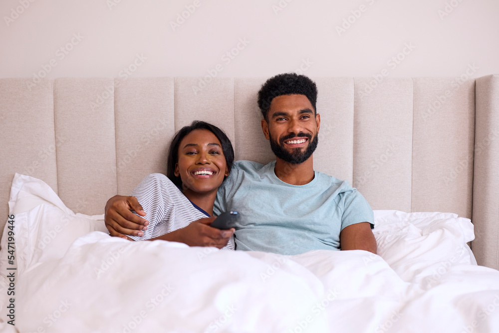 Fototapeta premium Loving Young Couple At Home Watching TV In Bed Together