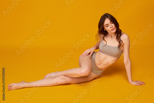 Fototapeta Naklejka Na Ścianę i Meble -  Portrait of young beautiful woman posing in grey underwear isolated over yellow studio background. Sensuality