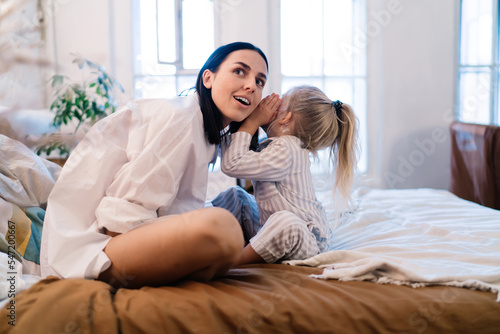 Daughter whispering secret to mother in bedroom