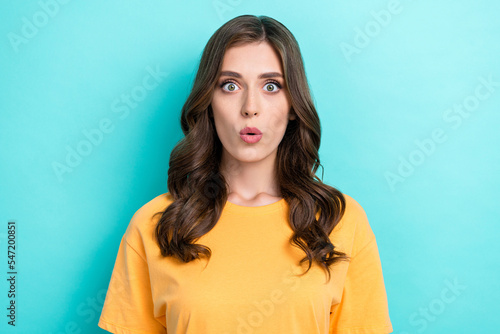 Photo of positive excited cute girl with wavy hairstyle wear yellow t-shirt impressed looking isolated on turquoise color background