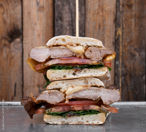 Gourmet sandwich. Closeup view of a multilayer sandwich with ciabatta bread, bondiola, cheese, arugula and onion, in a metal dish, with a wooden background.  photo