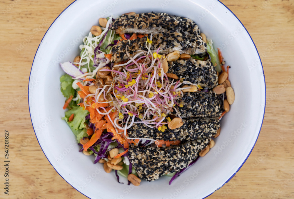 Healthy food. Top view of a salad with carrot, lettuce, peanuts, chicken breast breaded with seeds, soy sprouts and cabbage, in a white bowl on the wooden table. Healthy food. Top view of a salad with carrot, lettuce, peanuts, chicken breast breaded with seeds, soy sprouts and cabbage, in a white bowl on the wooden table.