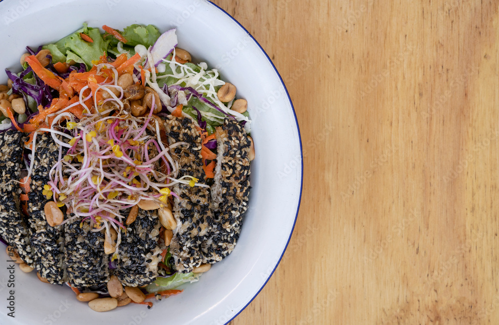 Healthy food. Top view of a salad with carrot, lettuce, peanuts, chicken breast breaded with seeds, soy sprouts and cabbage, in a white bowl on the wooden table. Healthy food. Top view of a salad with carrot, lettuce, peanuts, chicken breast breaded with seeds, soy sprouts and cabbage, in a white bowl on the wooden table.