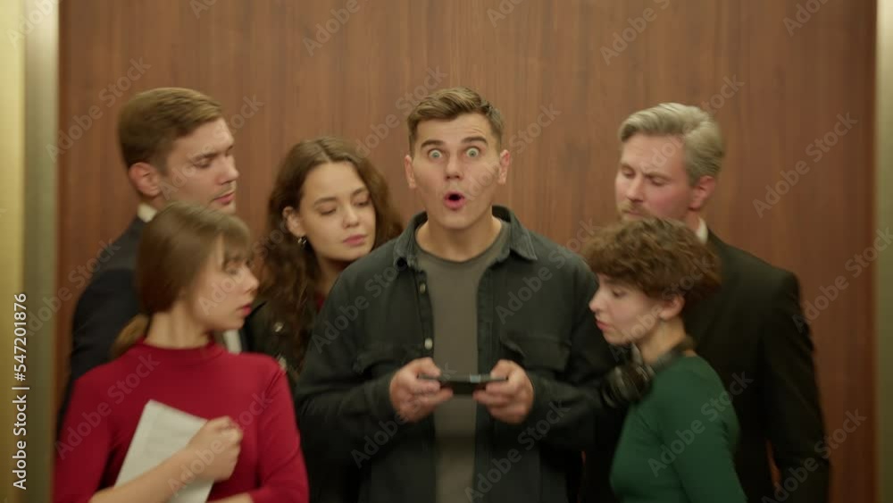 ZOOM IN Surprised man is using his smartphone in the elevator, everybody watching the screen ZOOM IN Surprised man is using his smartphone in the elevator, everybody watching the screen