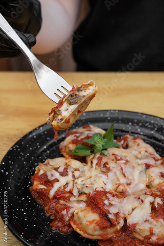 Stuffed pasta. Closeup view of a hand holding a fork, eating sorrentinos stuffed with cherry tomatoes and veal, with a mediterranean sauce and provolone cheese. photo