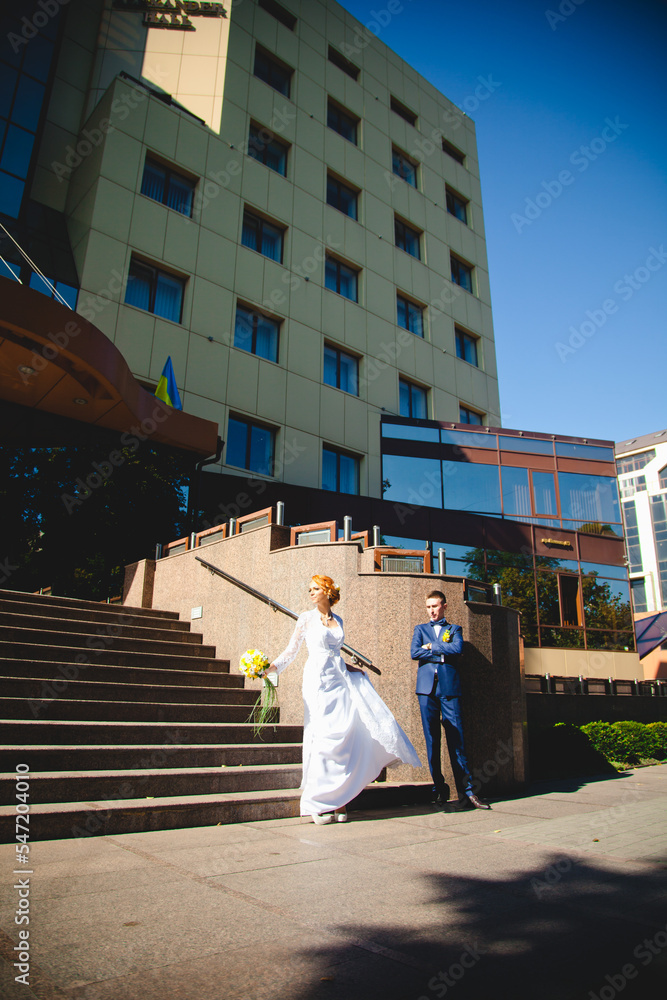 Obraz premium Young beautiful couple in a blue suit and white wedding dress with a bouquet