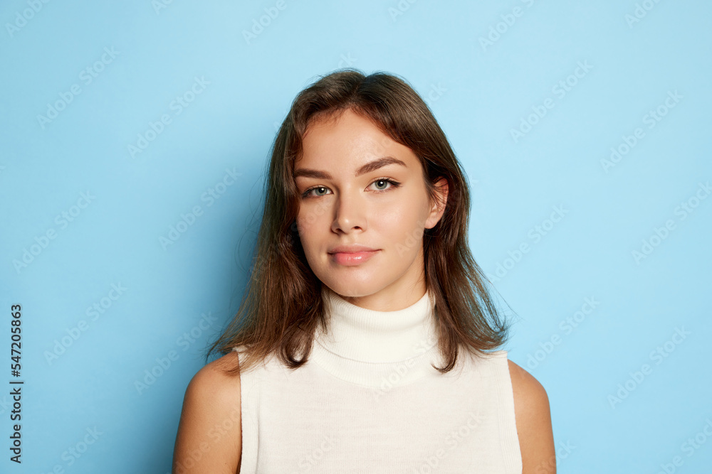 Portrait of young beautiful woman posing, looking at camera isolated over blue studio background. Attractive blue eyes Portrait of young beautiful woman posing, looking at camera isolated over blue studio background. Attractive blue eyes