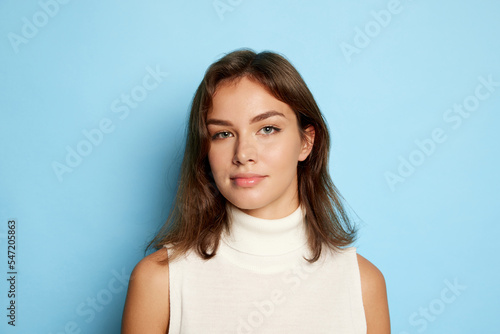Portrait of young beautiful woman posing, looking at camera isolated over blue studio background. Attractive blue eyes