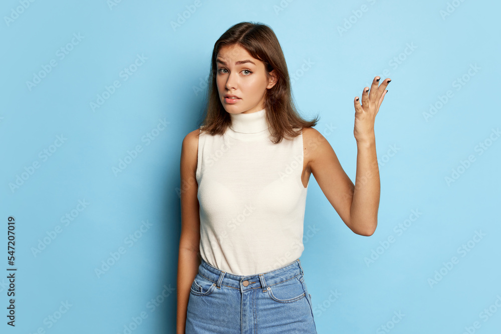 Portrait of young beautiful woman posing with questioning face isolated over blue studio background. Misunderstanding Portrait of young beautiful woman posing with questioning face isolated over blue studio background. Misunderstanding
