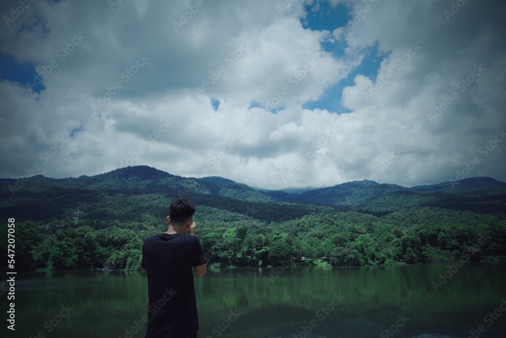 View from back of young man traveller using camera take a photo of  nature ,mountain ,lake and cloud
