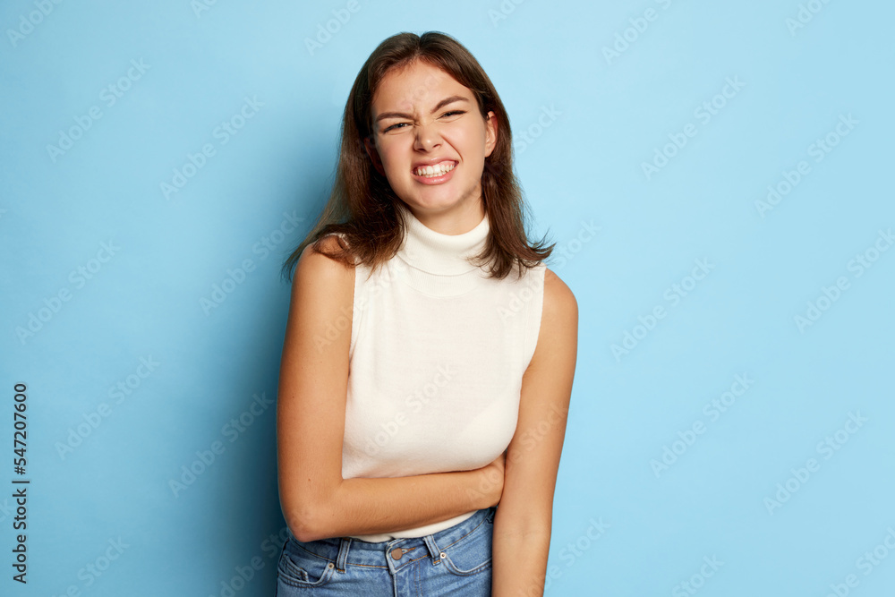 Portrait of young beautiful woman posing with funny smiling face isolated over blue studio background. Grimace Portrait of young beautiful woman posing with funny smiling face isolated over blue studio background. Grimace