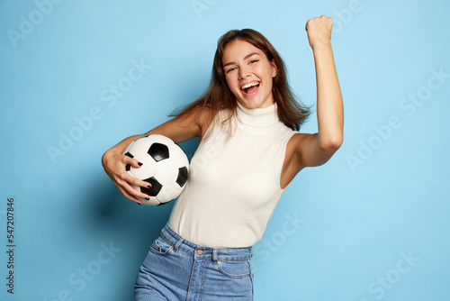 Portrait of young beautiful woman posing with happy winning look isolated over blue studio background. Football fan