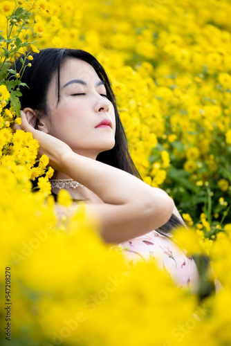 Beautiful girl hands up and lying on chrysanthemum flowers and enjoying warm sunlight. Asian woman smile and relaxing lying on the yellow flowers field. Woman among yellow blossom.