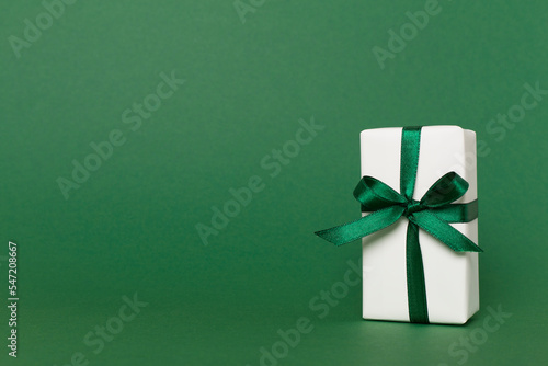 Gift box with green ribbon bow on color background