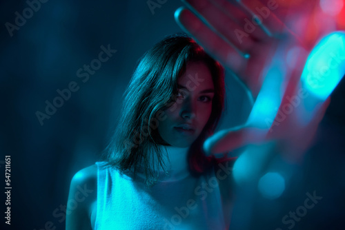 Portrait of young beautiful woman posing isolated over blue studio background in neon light. Bokeh effect
