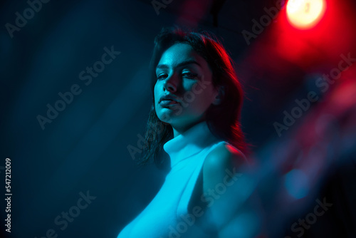 Portrait of young beautiful woman posing isolated over blue studio background in neon light. Nightclub lifestyle