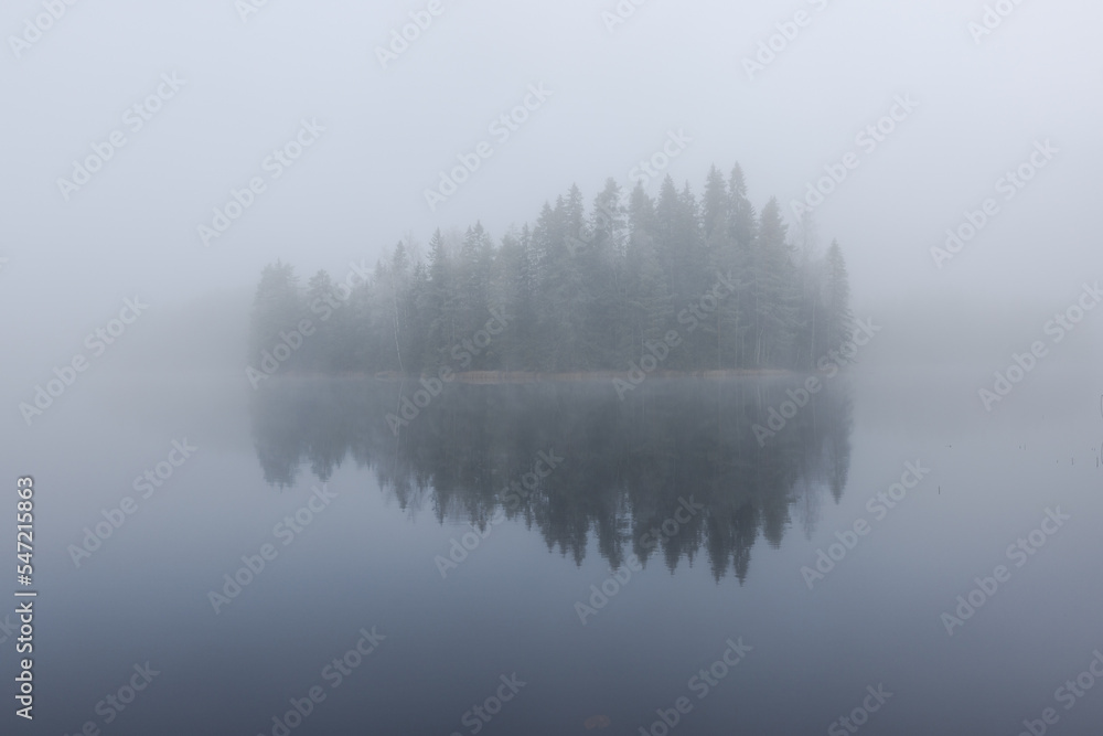 Foggy and cold late autumn morning by the lake in Finland. Island surounded by the fog.