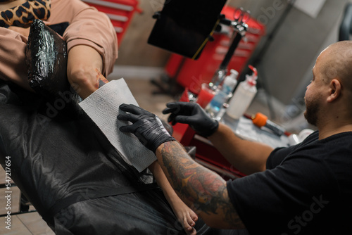 A male tattoo artist pulls a tattoo with a film to a client of a woman after a session