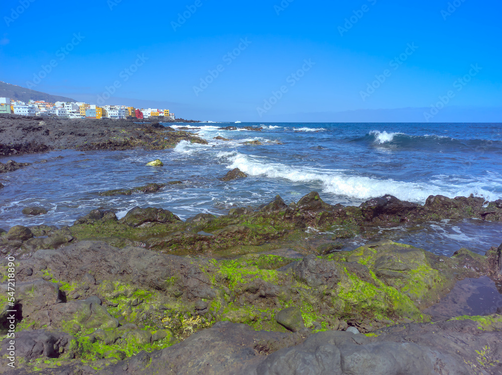 Playa Jardin with black and volcanic rocks. Colorful buildings in the distance. Puerto de la Cruz, Tenerife, Spain.