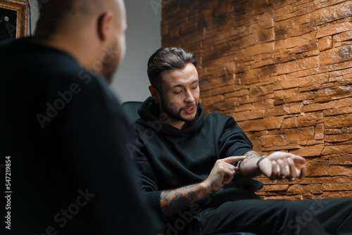 Interior of a tattoo studio - a man shows his tattoos to a master tattoo artist © Guys Who Shoot