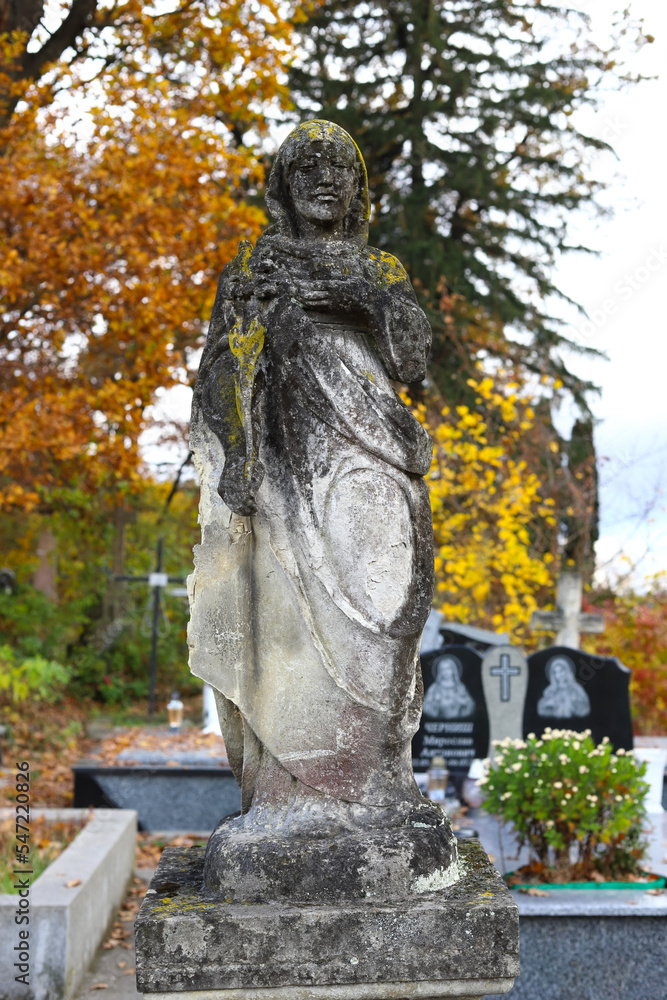 Fototapeta premium Old cemetery. Old neglected, mutilated figures of saints and crosses on graves. Remains of tombstones at a cemetery in Western Ukraine. Autumn sunny day.