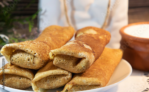 Homemade tasty thin rolled pancakes and a pot of sour cream 