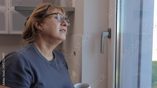 Mature Woman Holding a Cup of Tea or Coffee While Standing in Front of Windows During the Day photo