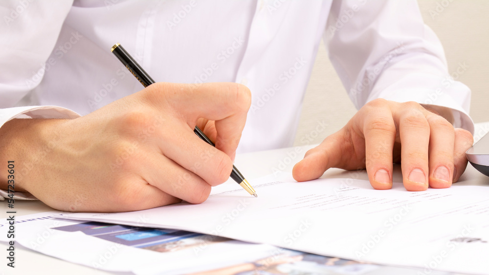 close shot of a human hand writing something on the paper. on the foreground magnifier glass, business concept close shot of a human hand writing something on the paper. on the foreground magnifier glass, business concept