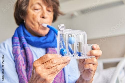 spirometer for breathing exercises. senior woman in hospital room practicing with spirometer photo